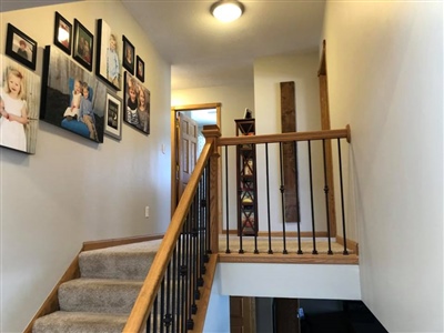 A carpeted staircase with wooden railings, leading to a landing area decorated with framed photos on the wall.