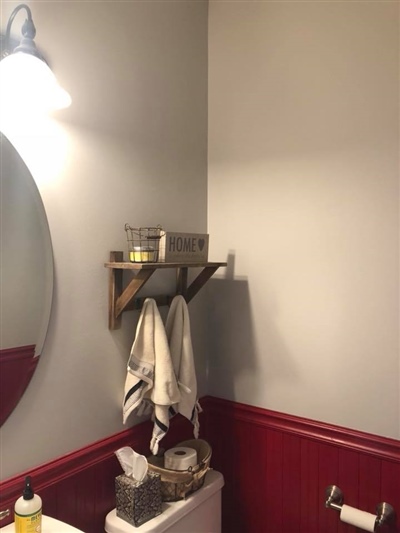 A bathroom with a round mirror, a wall-mounted light, a wooden shelf holding toiletries, white towels, and red wainscoting on the lower half of the walls.