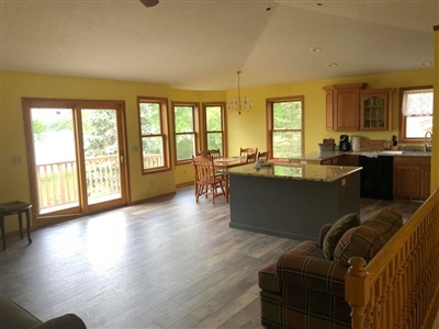 Open living area with yellow walls, large windows and glass doors leading to a deck, a kitchen island with seating, and a sofa in the corner.