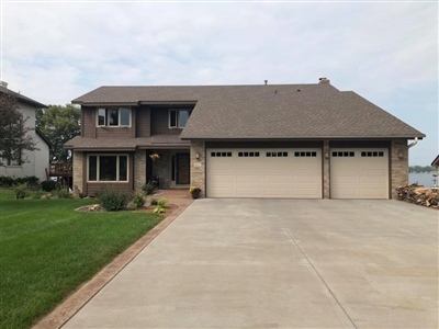 A two-story house with brown siding and a stone facade, a three-car garage, a concrete driveway, and a well-maintained lawn.