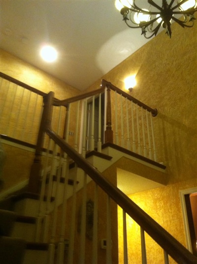 An indoor staircase with wooden railings, yellow walls, and a chandelier, illuminated by ceiling lights.