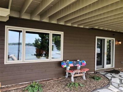 A patio area with brown siding, a large window, a glass door, a colorful bench, and a view of the lake in the background.