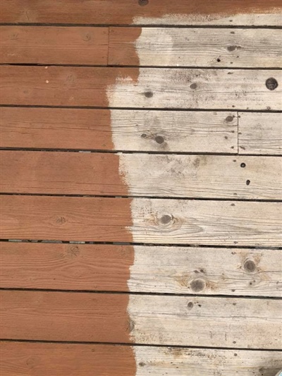 A wooden deck partially stained with reddish-brown paint, showing the contrast between the stained and unstained sections.