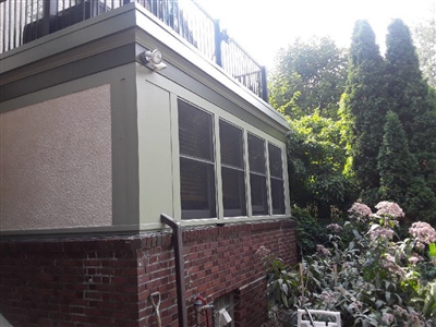 A house exterior with a mix of brick and stucco siding, a screened-in porch, and a garden with flowering plants and tall evergreens.