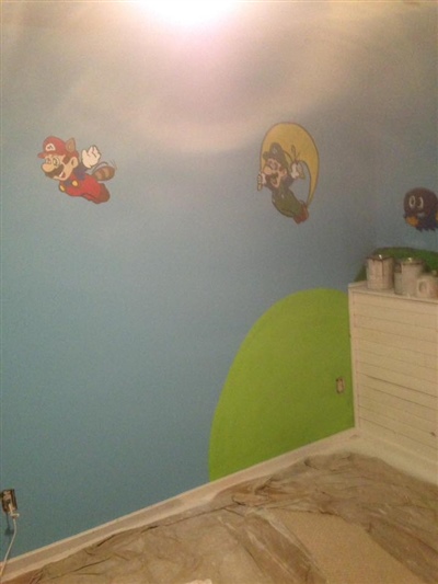 A room with blue walls featuring Mario-themed wall decals, a green hill mural, and a white dresser in the corner.