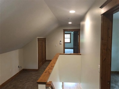 An upstairs hallway with sloped ceilings, wooden trim, carpeted flooring, recessed lighting, and doorways leading to adjacent rooms.