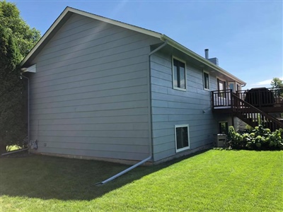 Side view of a two-story house with blue siding, a well-maintained lawn, and a wooden deck at the back.