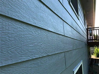 Close-up view of blue horizontal siding on a house, with a glimpse of a wooden deck and railing in the background.