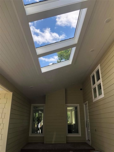 A covered outdoor area with pale yellow siding and two large skylights in the ceiling, providing a view of the blue sky and clouds.