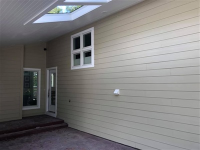 A covered outdoor area with pale yellow siding, a skylight, a white door, and windows, leading to a patio space.