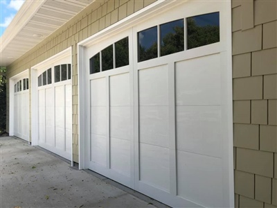 A row of white garage doors with upper windows, set against light yellow siding.