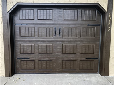 A brown garage door with decorative panels and black hardware, set in a beige exterior.