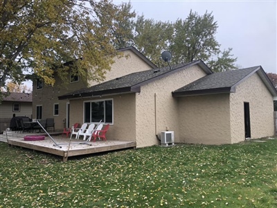 A beige house with a wooden deck in the backyard, surrounded by a grassy lawn and trees with autumn foliage.