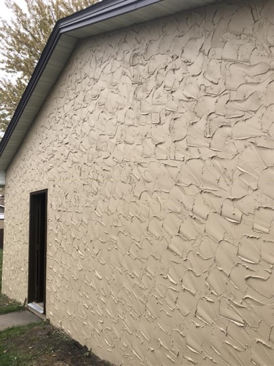 A beige stucco wall with a textured finish and a small open doorway, under a dark-colored roof.