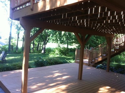 A wooden deck with a pergola, supported by wooden posts, overlooking a lush green backyard with trees.