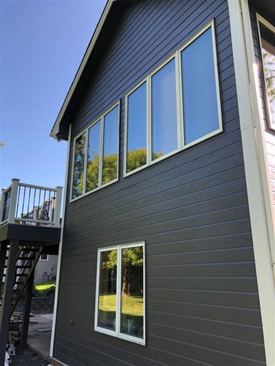 Side view of a gray house with multiple large windows on the upper and lower floors, and an exterior staircase leading to a balcony.