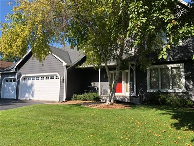 Front view of a gray house with a red front door, large windows, a two-car garage, and a well-maintained lawn with trees.