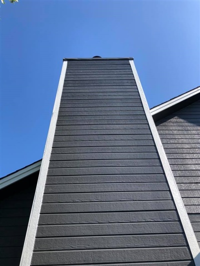 Close-up view of a tall, gray house chimney with white trim, extending into a clear blue sky.