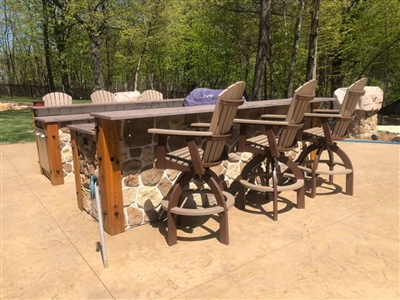 Outdoor bar with high wooden stools, a stone base, and a countertop, set on a concrete patio with trees in the background.