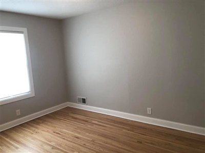 Empty room with light wood flooring, gray walls, white trim, and a window on the left side.