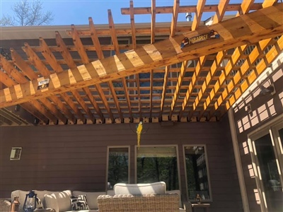 Outdoor patio with wooden pergola, outdoor furniture, and sliding glass doors, under a clear blue sky.