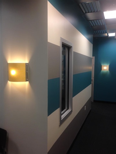 Hallway with striped walls in shades of teal, gray, and white, featuring modern wall sconces and a window.