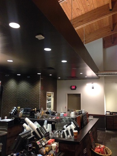 Coffee shop counter area with a dark ceiling, recessed lighting, and various coffee-making equipment, set against a backdrop of dark brick walls and wooden accents.