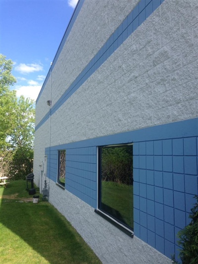 Side view of a commercial building with blue and white walls, large windows, and green grass, under a clear blue sky.