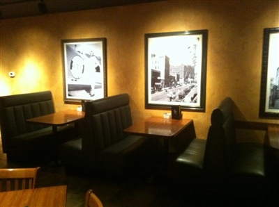 Dimly lit restaurant with black leather booth seating, wooden tables, and framed black-and-white photographs on the walls.