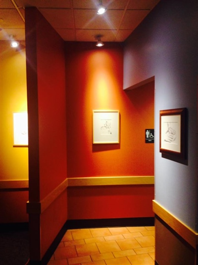 Hallway with brightly colored walls in red, orange, and purple, featuring framed artwork and recessed lighting.