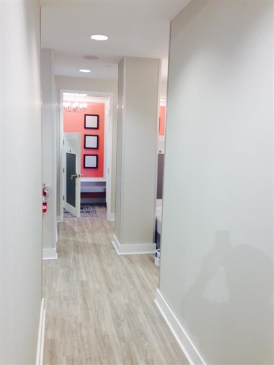 Bright hallway with light wood flooring, white walls, and an orange accent wall in the background featuring framed artwork.