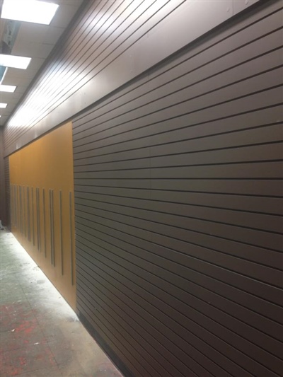 Hallway with dark brown paneled walls and bright overhead lighting, featuring a contrasting section with vertical slats.