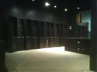 An empty, dark-colored room with built-in shelving and drawers, illuminated by overhead spotlights.