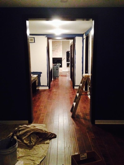 A hallway in a house under renovation, with wooden floors, dark walls, and construction materials scattered around.