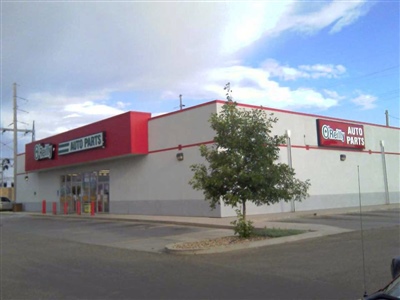 A standalone AutoZone store with a red and white exterior, located in a parking lot with a small tree in front.