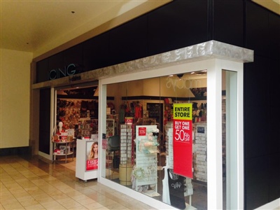 A mall retail store with a black exterior, large display windows showcasing various products, and sale signs in the window.