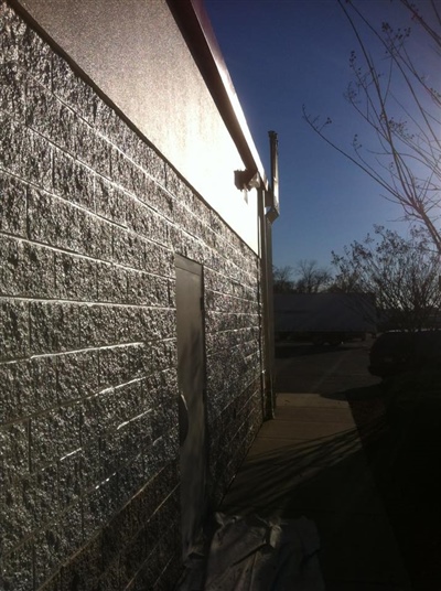 A side view of a building with a textured brick wall, a security camera, and a clear sky in the background.