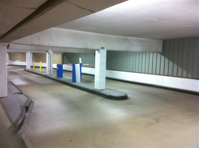 An empty underground parking garage with white columns, yellow and blue parking meters, and concrete floors.