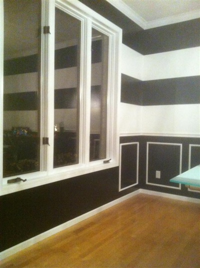 A room with bold black and white striped walls, large windows, and wooden floors.