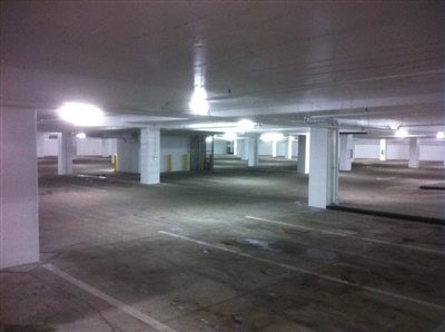 An empty underground parking garage with white columns, low ceilings, and overhead lighting.