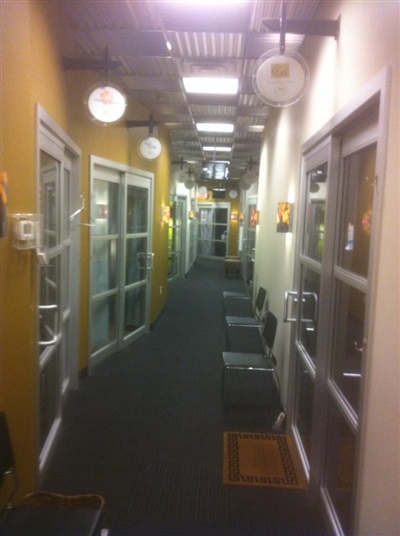 A long hallway with glass doors on both sides, overhead lights, and chairs placed along the walls.