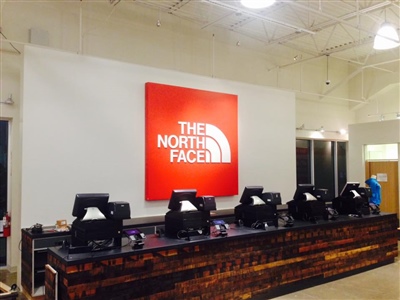 A store checkout area with multiple registers and a large red North Face logo on the wall behind the counter.