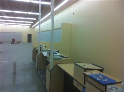 An empty retail space with checkout counters, light yellow walls, and overhead fluorescent lighting.