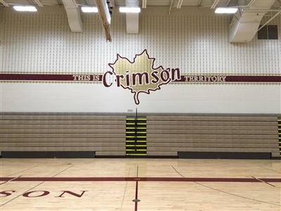 A high school gymnasium with a logo that reads "Crimson" on the wall, bleachers, and a basketball court floor.