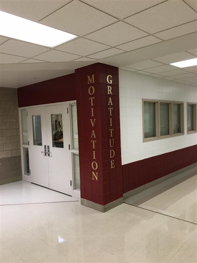 A school hallway with a maroon column displaying the words "Motivation" and "Gratitude," next to white doors and windows.