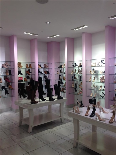 A shoe store with white shelves and tables displaying various types of footwear, featuring light pink columns and bright lighting.