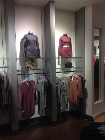 A clothing store display featuring mannequins dressed in sweaters, with matching garments hanging below on glass shelves, and a full-length mirror on the side.