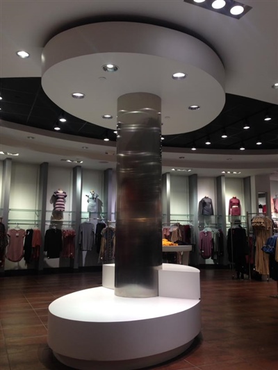 A retail store interior with a central illuminated column surrounded by circular display platforms, and racks of clothing neatly arranged in the background.