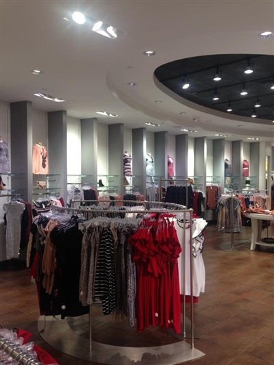 A retail clothing store with neatly arranged racks displaying various garments, bright lighting, and a modern interior design with circular ceiling features.