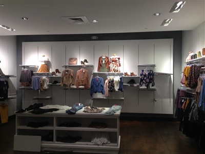 A clothing store display with neatly arranged shelves and racks showcasing various apparel, illuminated by overhead lights.